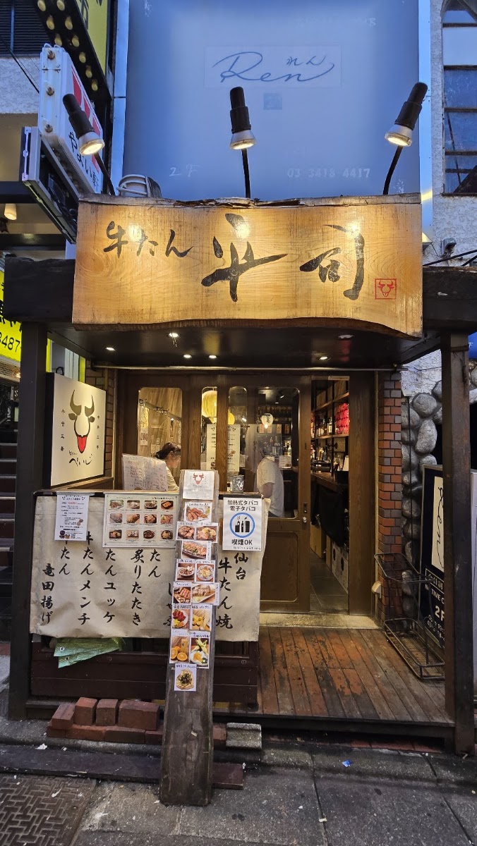 夜の店先。無垢板の看板に「牛たん 平司」と筆文字で書かれ、上から二灯のスポットライトが当たっている。牛の顔を描いた白い提灯と、手書きの紙が縦に並ぶ。