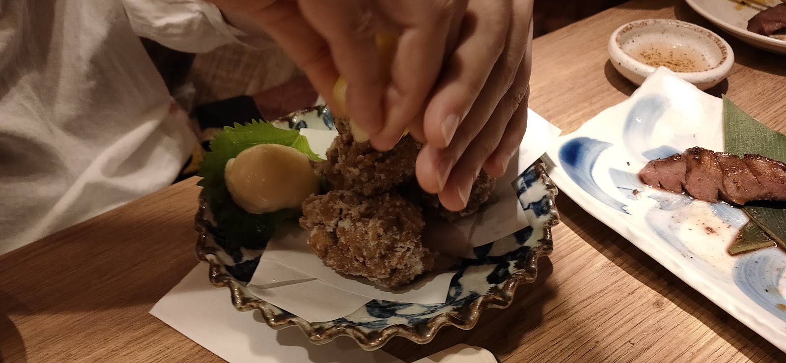 青と白の皿にのった料理に、手がレモンをしぼっているところ。